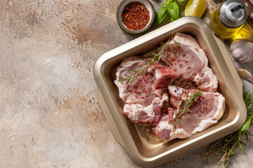Fresh raw pork loin on the bone with spices and marinade on a stone tabletop, preparation for baking or barbecue. Top view flat lay background. Copy space.