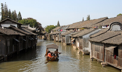 Obraz premium Wuzhen Water Town, Zhejiang Province, China. A small boat carrying tourists explores the old town and canals of Wuzhen. Unrecognizable people.