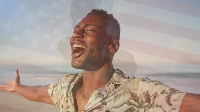 Animation of flag of united states of america over happy african american man on beach