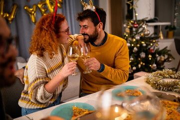 Young smiling couple holding glasses with white wine and looking each other during Christmas dinner or lunch.