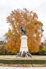 sculpture of the fallen angel or devil in Retiro park with trees in autumn colors