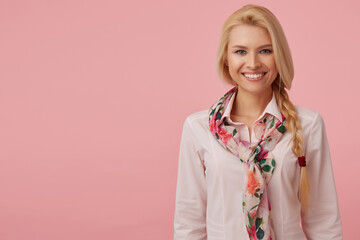 Studio Portrait of blonde female wears pastel pink shirt and bright neckerchief smiling while looking into camera. isolated over pink background