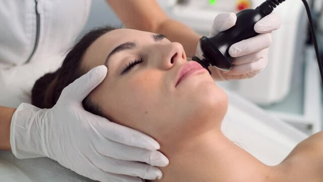 Video of cosmetologist makes the procedure an ultrasonic cleaning of the facial skin of a beautiful young woman on the spa center.
