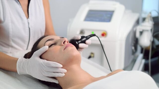 Video of cosmetologist makes the procedure an ultrasonic cleaning of the facial skin of a beautiful young woman on the spa center.
