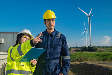 Two engineers working and holding the report at wind turbine farm Power Generator Station on mountain,Thailand people,Technician man and woman discuss about work