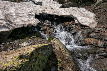 a mountain stream flows out from under a glacier