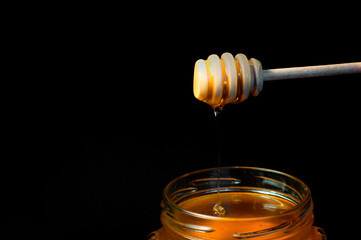 honey flows on a wooden spoon in a jar on a black background. High quality photo