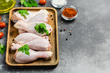 Raw chicken legs, parsley, olive oil, tomatoes on wooden tray on dark background. Top view, copy space.