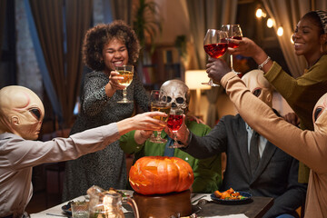 Group of of happy friends toasting with glasses of red wine and celebrating Halloween during home...
