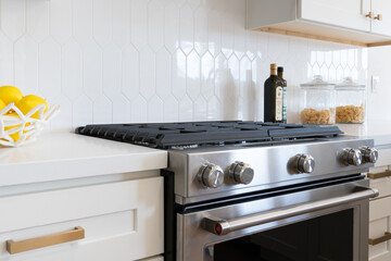 Modern kitchen details of white marble counter, gas stove, and white tile backsplash.