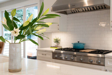Modern kitchen detail of large flower arrangement in front of double gas stove top with turquoise...