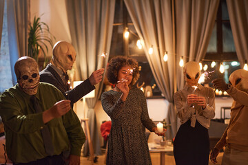 Group of people in scary masks holding sparklers and dancing during Halloween party
