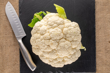 One ripe cauliflower with a knife on a slate stone, close-up, top view.