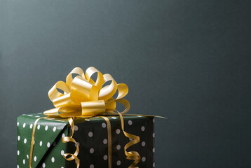Gift in green polka dot packaging with a golden bow on a blue-green background