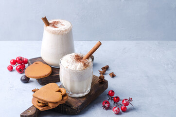 Milk-egg drink with thick foam, cinnamon and gingerbread on a light background, selective focus