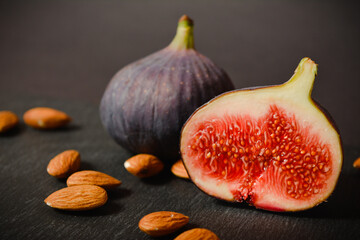 Close up of half of Azerbaijani fig fruit and one whole berry on background out of focus. Exotic eastern fruit with almonds. Segmented berry with almond fruits isolated on black stone background
