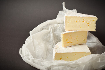 Close up of soft French Brie cheese pieces on white parchment paper on dark background. Three pieces of cheese
