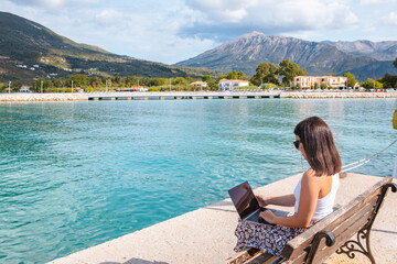 Fototapeta premium smiling woman freelancer working on laptop outdoors at city harbor
