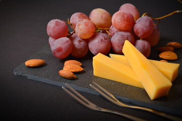 Side view of French hard cheese cheeseboard with pink grape and almond nuts on black slate stone...