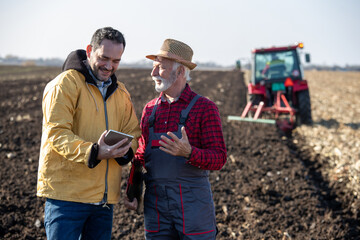 Farmers talking in field in front of tractor in autumn