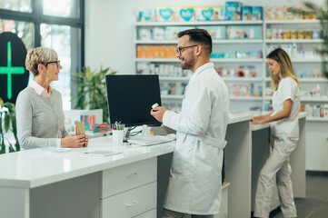 Obraz premium Young male pharmacist giving prescription medications to senior female customer in a pharmacy