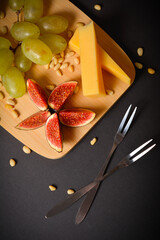 Top view of cheeseboard with pine nuts on black background. Hard French cheese pieces with green...