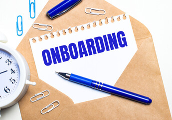 On a light background, a craft envelope, an alarm clock, paper clips, a blue pen and a sheet of...