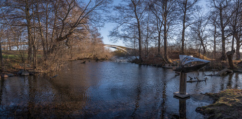 Water front view at the public beach Smedsuddsbadet, lagun with metal figure called Fiskfosil, long bridge Västerbron in the background a sunny color full autumn day in Stockholm
