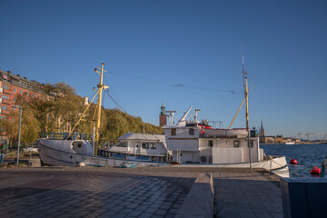 Various boats at the pier Norrm&auml;larstrand at the bay Riddarfj&auml;rden in the district Kungsholmen, the tower of the Town City Hall a sunny color full autumn day in Stockholm