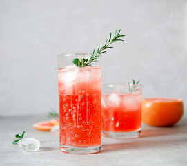 Refreshing drink with grapefruit juice and basil seeds, a sprig of rosemary, ice cubes on a gray background.