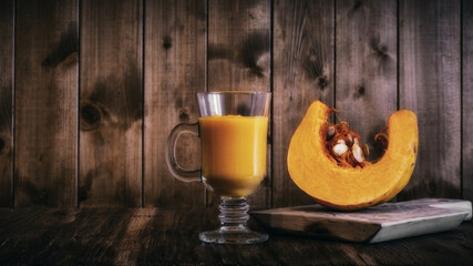pumpkin smoothie with a transparent glass with a crescent-shaped pumpkin slice on a cutting board on a soft wooden background. side view. simple still life in rustic style with copy space