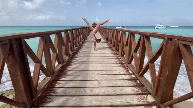 Flexible female circus doing handstand on the pier with sky and sea background. Individuality, outstanding and originality.