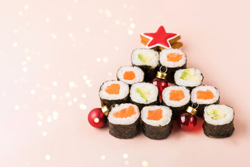 Fresh sushi roll with salmon and avocado in a pyramid isolated on soft pink background with Christmas decorations. Traditional japanese food. Flat lay style.
