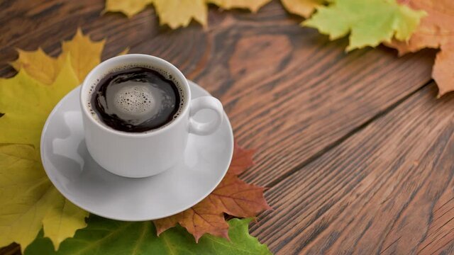 coffe cup on wooden table with colorful autumnal maple leaves with spinning coffee bubbles