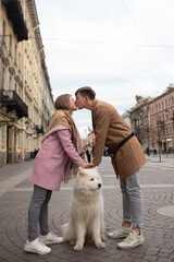 a couple in love a guy and a girl are walking in the parks of a beautiful city in autumn in November with a friend of a white fluffy big dog