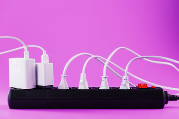 Electric mains filter with inserted white plugs of electrical appliances on a pink background.