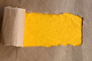 Brown paper flat lay with strip torn horizontally to reveal bright yellow copy space for advertising.
