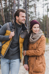 Fototapeta premium happy young couple in autumn outfit looking away while walking in forest