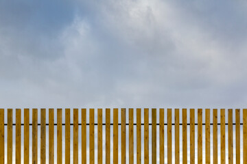 New wooden fence against the backdrop of the daytime cloudy sky.