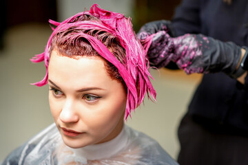 The professional hairdresser uses a brush to apply the pink dye to the hair. Hair coloring concept