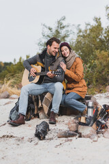 happy man leaning on man playing guitar while sitting near bonfire