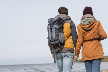 back view of couple in autumn outfit holding hands while hiking near river