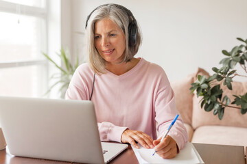 Middle aged businesswoman using earphone while sitting behind her laptop
