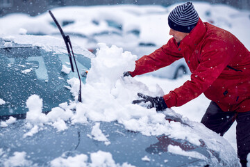 Winter problems of car drivers. man brushing the snow off his car on a  winter day