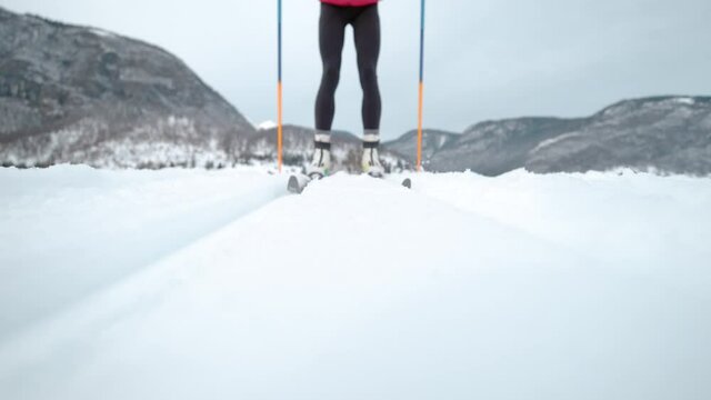 SLOW MOTION, LOW ANGLE, CLOSE UP, DOF: Young Caucasian woman nordic skiing in the Slovenian mountains pushes herself along the tracks. Female athlete skis along tracks running around a training center