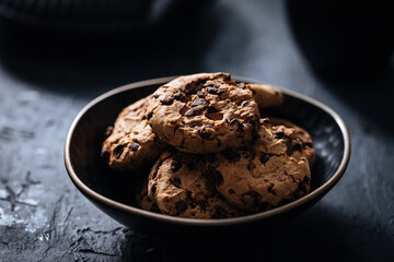 Chocolate chip cookies with tea in background in a dark moody atmosphere 