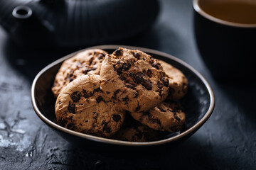 Chocolate chip cookies with tea in background in a dark moody atmosphere 