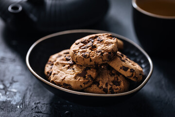 Chocolate chip cookies with tea in background in a dark moody atmosphere 