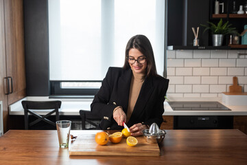 Obraz na płótnie Canvas Young business woman making morning vitamin bomb energy drink juice in the kitchen from orange fruit and lemon before she go to the work. Female person healthy life concept.