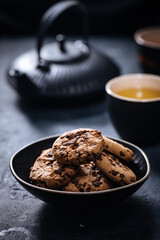 Chocolate chip cookies with tea in background in a dark moody atmosphere 